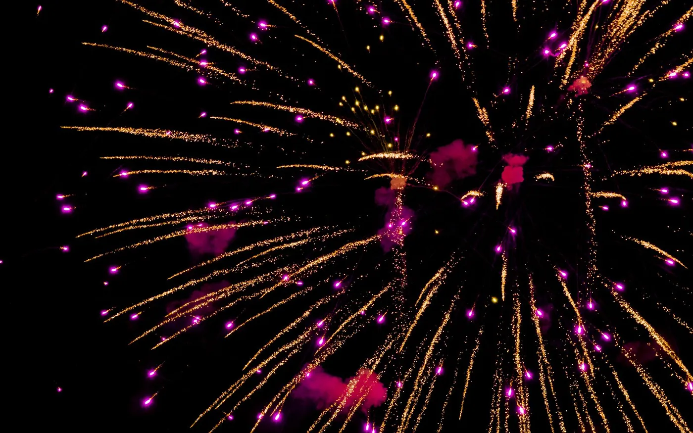 Fogos de artifício roxos e amarelos explodindo no céu à noite
